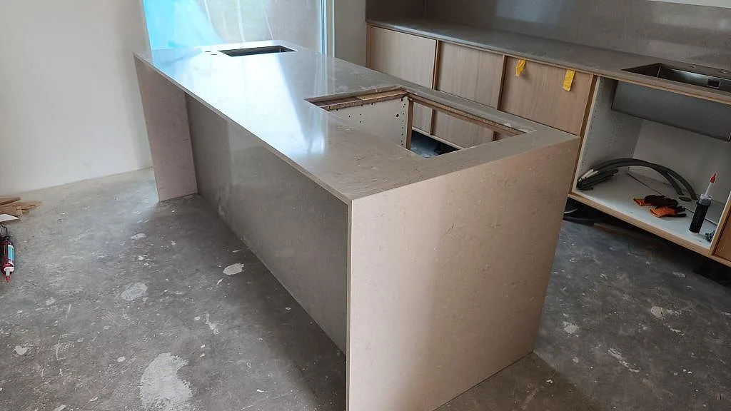 Köksödel i polerad Silestone Coral Clay, kvartskomposit, med rektangulära urtag och ljusa köksstommar under montering i Lomma.
