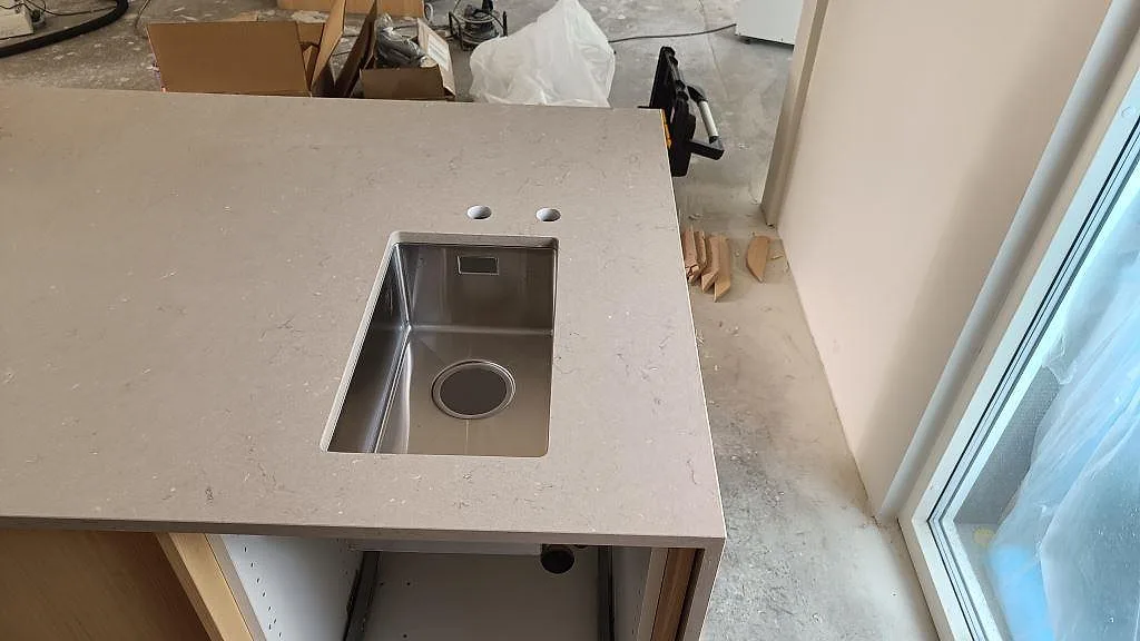 Polerad Silestone Coral Clay bänkskiva i kvartskomposit med synlig diskho, dubbla kranhål och ljus träinredning under montering i Lomma.
