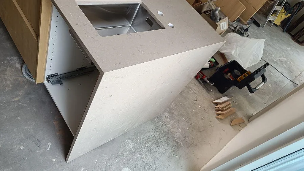Detalj av köksö i polerad Silestone Coral Clay, kvartskomposit, med synlig diskho och stenklädd sida i ett kök i Lomma.