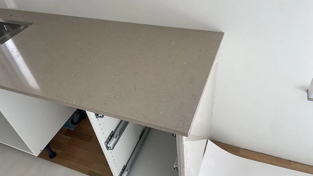 Detalj av polerad Silestone Coral Clay köksbänkskiva vid diskzonen, med greige kvartskomposit och synlig kant i Lomma.