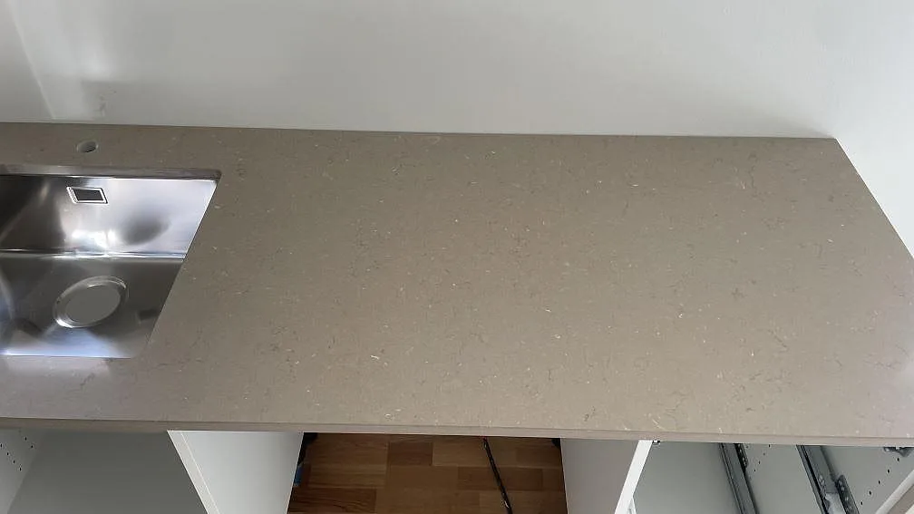 Lång köksbänkskiva i polerad Silestone Coral Clay med rostfri diskho och borrat kranhål längs väggen i ett kök i Lomma.
