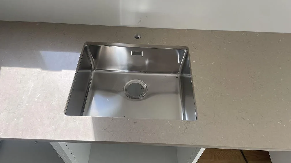 Underlimmad rostfri diskho i en polerad köksbänkskiva av Silestone Coral Clay med borrat kranhål i Lomma.