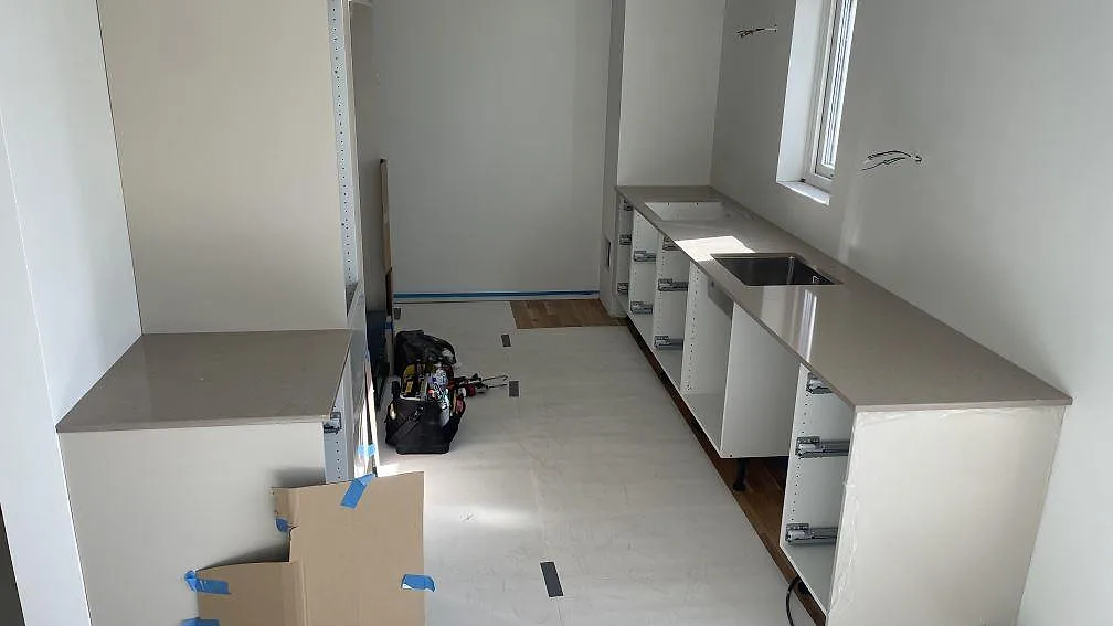 Köksbänkskiva i Silestone Coral Clay, polerad greige kvartskomposit, monterad längs två väggar med rostfri diskho och urtag för häll i ett kök i Lomma.
