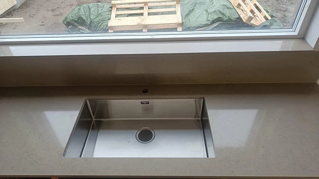 Närbild på polerad Silestone Coral Clay som köksbänkskiva med underlimmad rostfri diskho och matchande stänkskydd vid fönster i Lund.