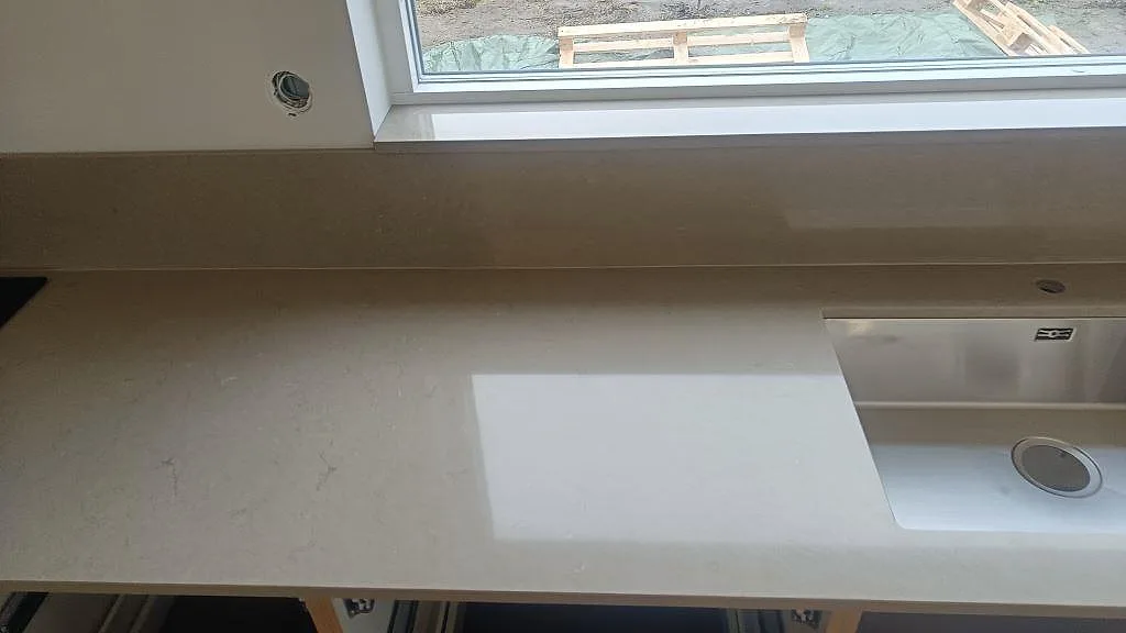 Polerad kvartskomposit i Silestone Coral Clay med rostfri diskho, uppvikt stänkskydd och ljus fönsterreflex i ett kök i Lund.