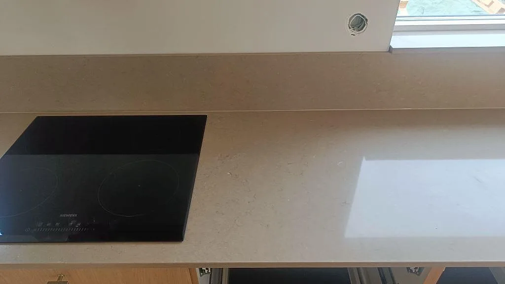 Polerad bänkskiva i Silestone Coral Clay med infälld svart häll, ljus fönsterreflex och öppna köksstommar i Lund.