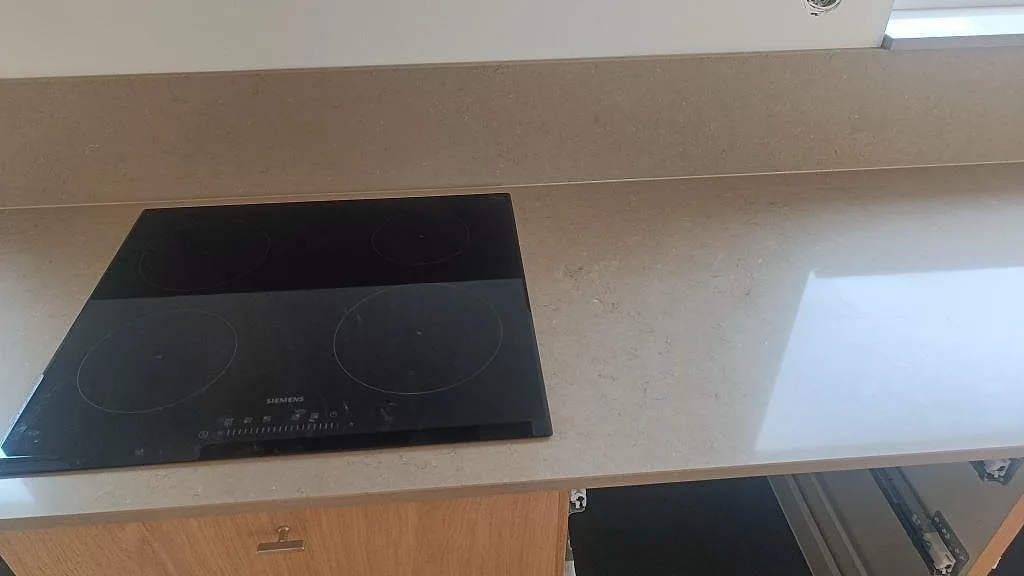 Detalj av polerad Silestone Coral Clay runt svart häll och uppvikt stänkskydd under fönster i Lund.