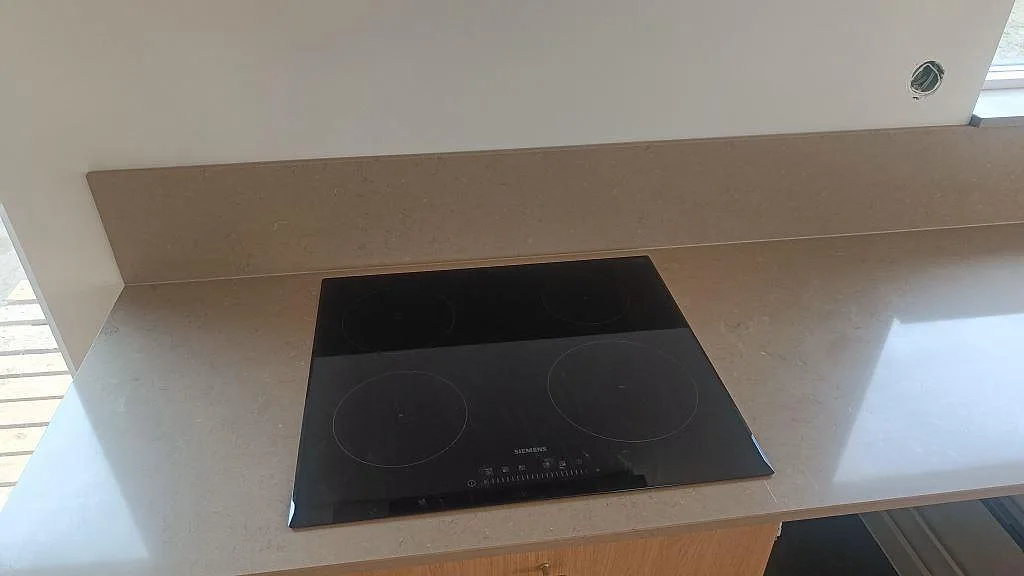 Svart häll monterad i polerad Silestone Coral Clay med matchande stänkskydd och träinredning i kök i Lund.