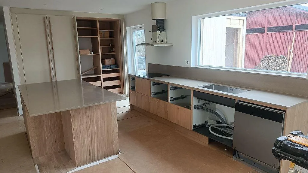 Polerad köksbänkskiva i Silestone Coral Clay med träklädd köksö, rak bänksträcka, rostfri diskho och häll i ett kök i Lund.