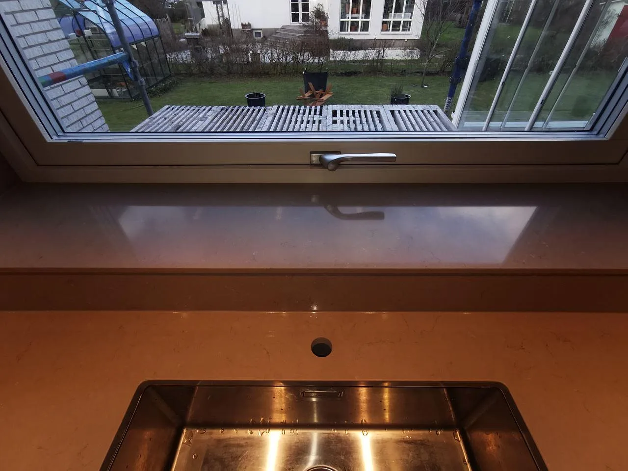 Polerad Silestone Coral Clay köksbänkskiva med underlimmad rostfri diskho och stenklädd fönsterbänk i ett kök i Malmö.