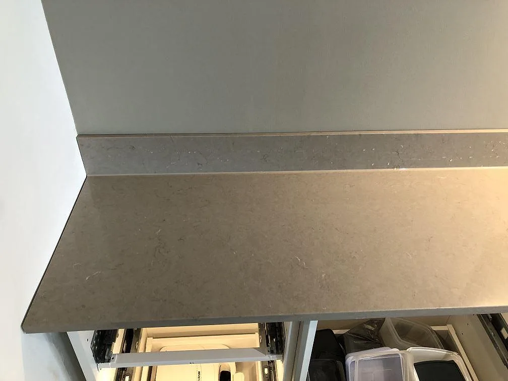 Detalj av matt greige köksbänkskiva i Silestone Coral Clay med låg uppvikt stänkkant mot väggen i ett kök i Malmö.