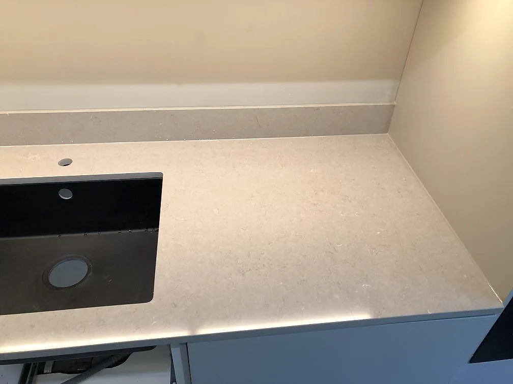 Närbild på underlimmad svart diskho i en köksbänkskiva i Silestone Coral Clay, matt greige kvartskomposit, i ett kök i Malmö.