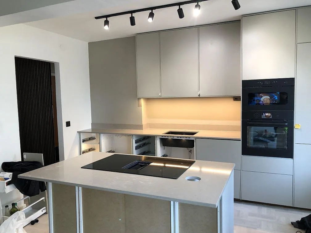 Köksbänkskiva i Silestone Coral Clay, varm greige matt kvartskomposit, i ett vinkelkök i Malmö med separat köksö, mörk induktionshäll och ljusa gröngrå skåp.