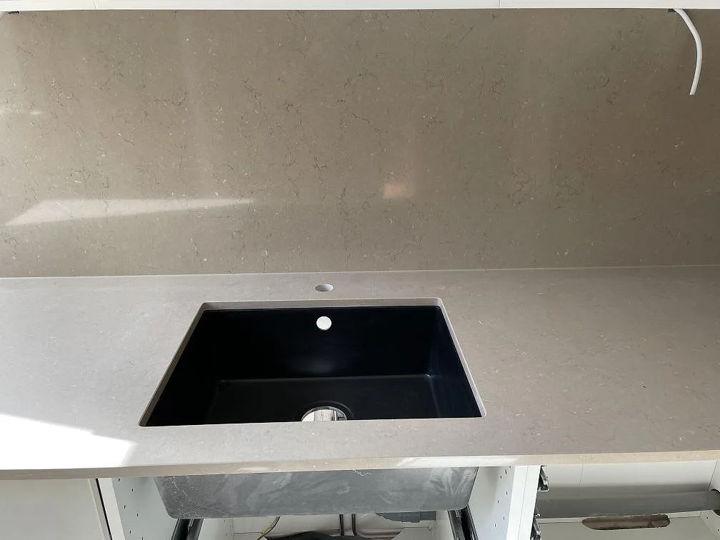 Silestone Coral Clay bänkskiva och heltäckande stänkvägg i Malmö med svart induktionshäll och integrerad fläkt i cremevita överskåp.