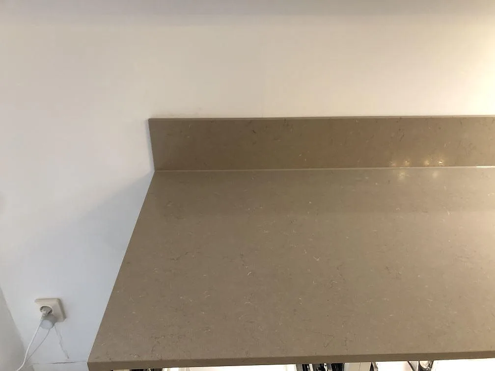 Installerad köksbänkskiva i polerad Silestone Coral Clay med uppvikt stänkkant mot vit vägg i ett kök under montering i Malmö.