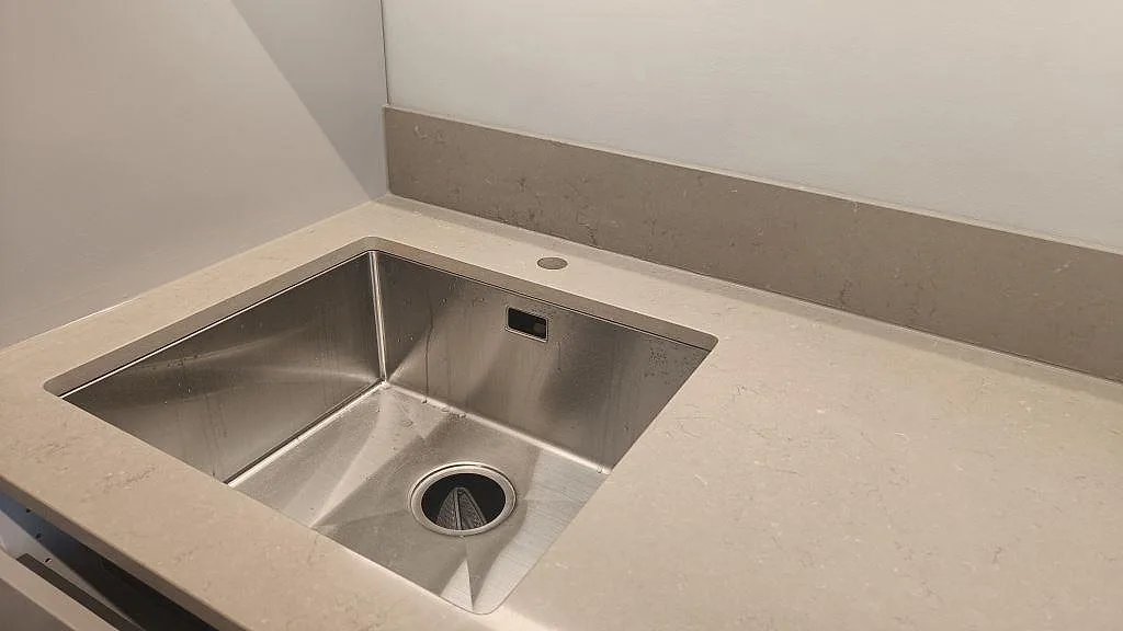 Underlimmad rostfri enkelho infälld i matt Silestone Coral Clay bänkskiva med uppvikt stänkkant, närbild i ett kök i Malmö.
