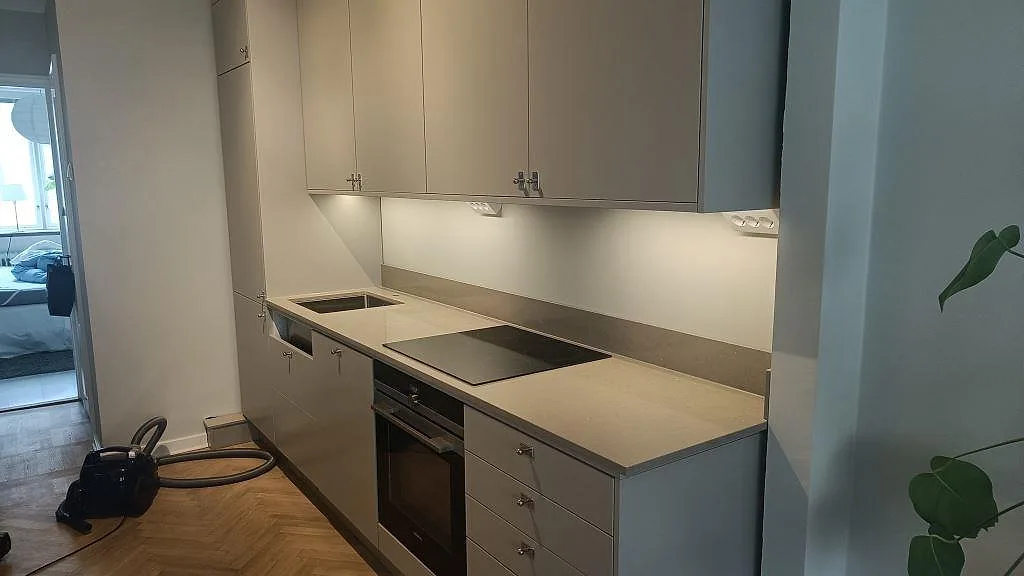 Köksbänkskiva i Silestone Coral Clay, matt taupe kvartskomposit, installerad längs väggen i ett enkelradigt kök i Malmö med underlimmad rostfri diskho, induktionshäll och inbyggd ugn.