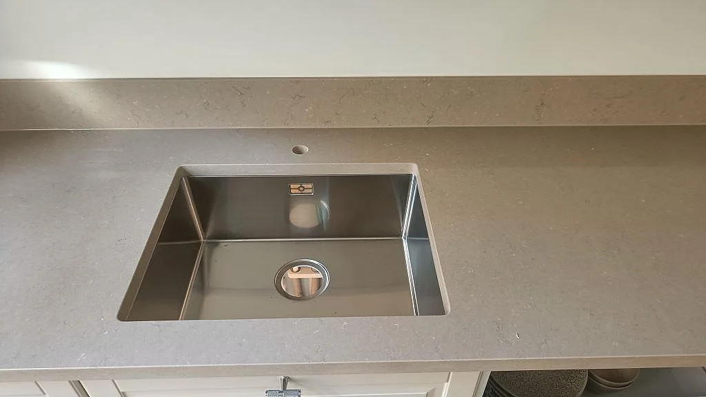 Detalj av underlimmad rostfri diskho med borrat blandarhål i en matt Silestone Coral Clay bänkskiva i ett kök i Malmö.