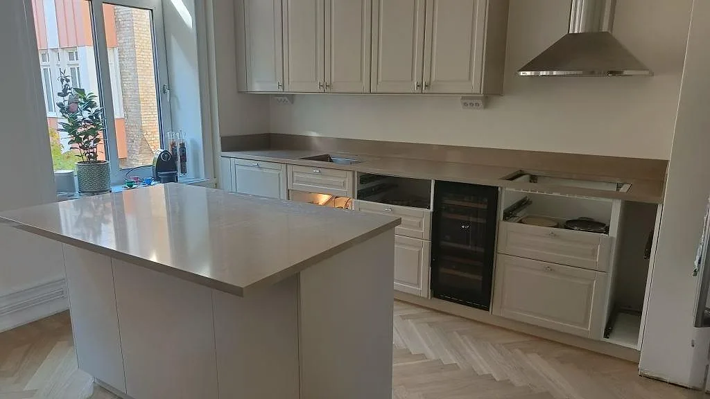Köksbänkskiva och köksö i Silestone Coral Clay, en matt taupe kvartskomposit, i ett ljust greige kök med fiskbensparkett och rostfri spiskåpa i Malmö.