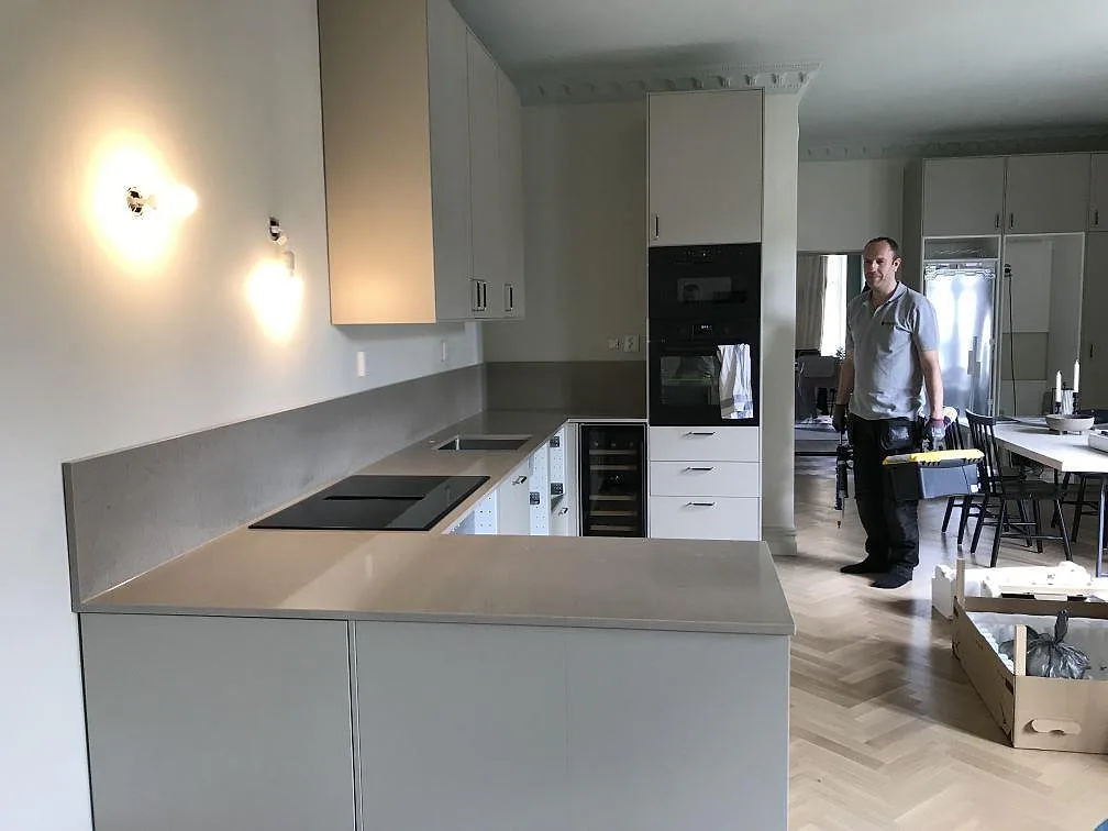 Köksbänkskiva i varmt greige Silestone Coral Clay, matt, i ett U-format kök i Malmö med greppfria ljusgrå luckor, induktionshäll och uppvikt stänkkant.