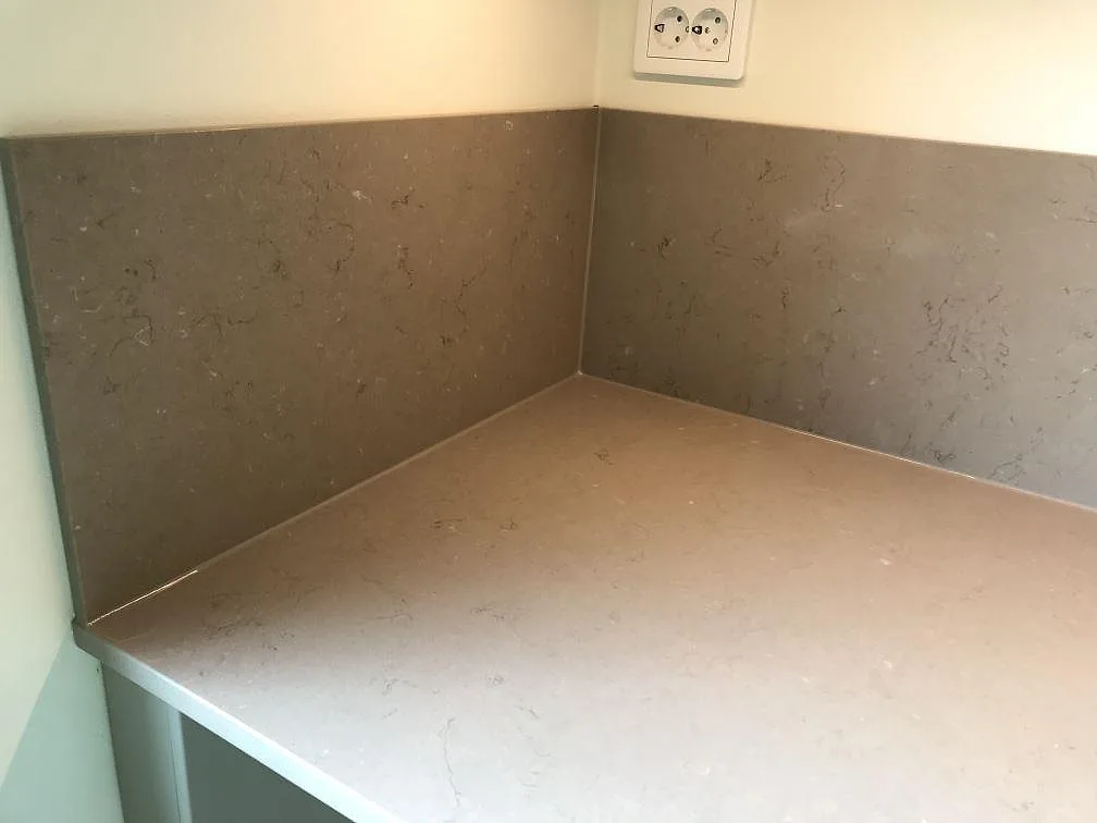 Heltäckande stänkvägg i Silestone Coral Clay ovanför köksbänkskivan, med diskret ådring i den taupe kvartskompositen, i ett kök i Malmö.