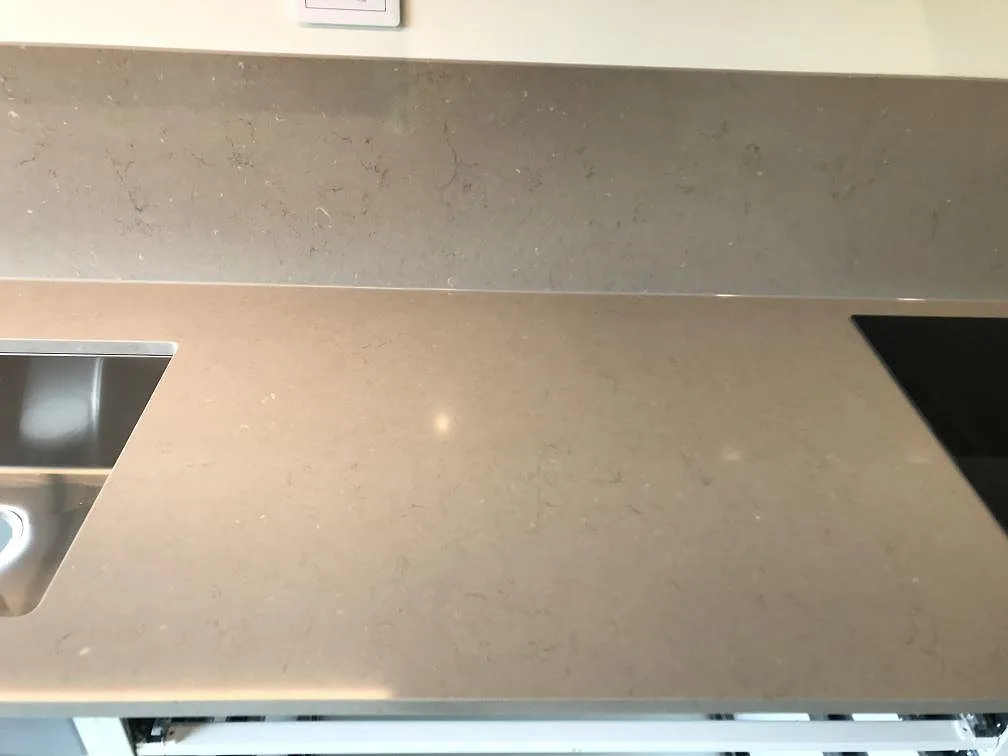 Köksbänkskiva i polerad Silestone Coral Clay med infälld induktionshäll och underlimmad rostfri diskho längs en lång bänkrad i ett kök i Malmö.