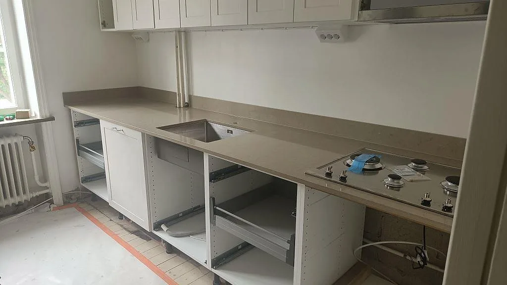 Köksbänkskiva i Silestone Coral Clay, polerad greige kvartskomposit, monterad i en lång L-bänk med underlimmad rostfri diskho och infälld gashäll i ett kök i Malmö.