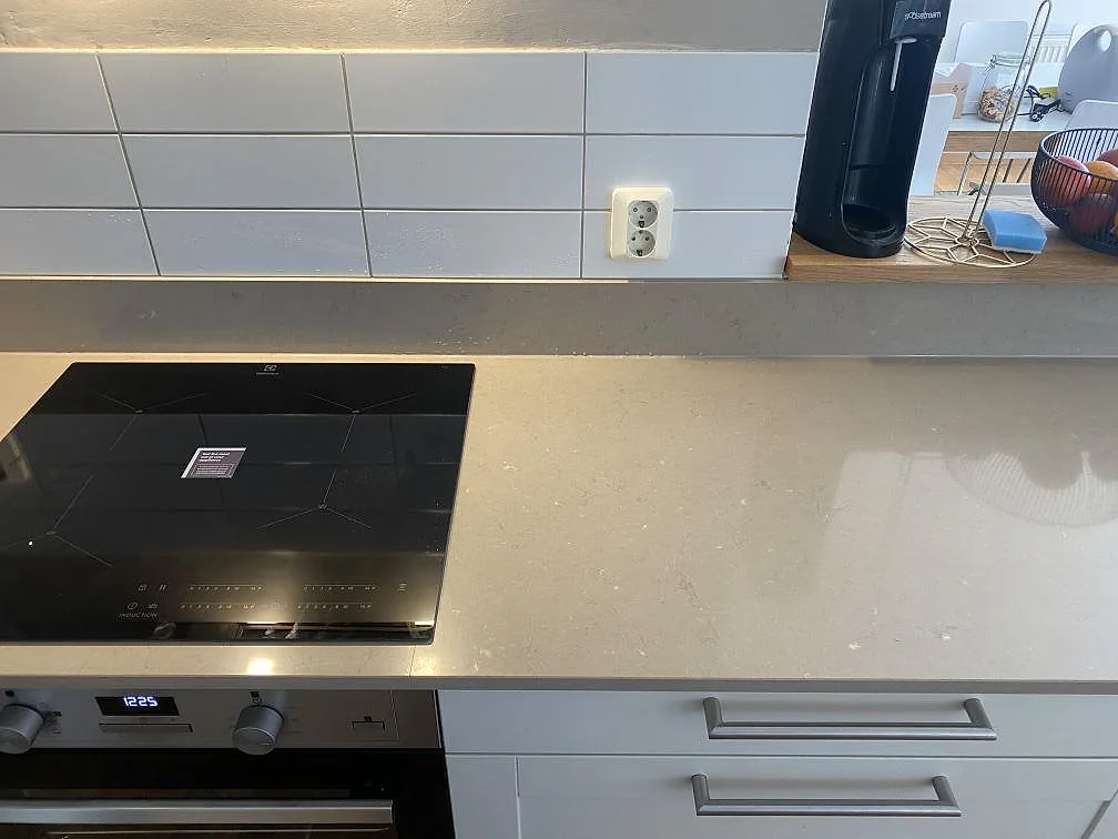 Beige bänkskiva i Silestone Coral Clay med svart induktionshäll och vitt kakel ovanför i ett kök i Malmö.