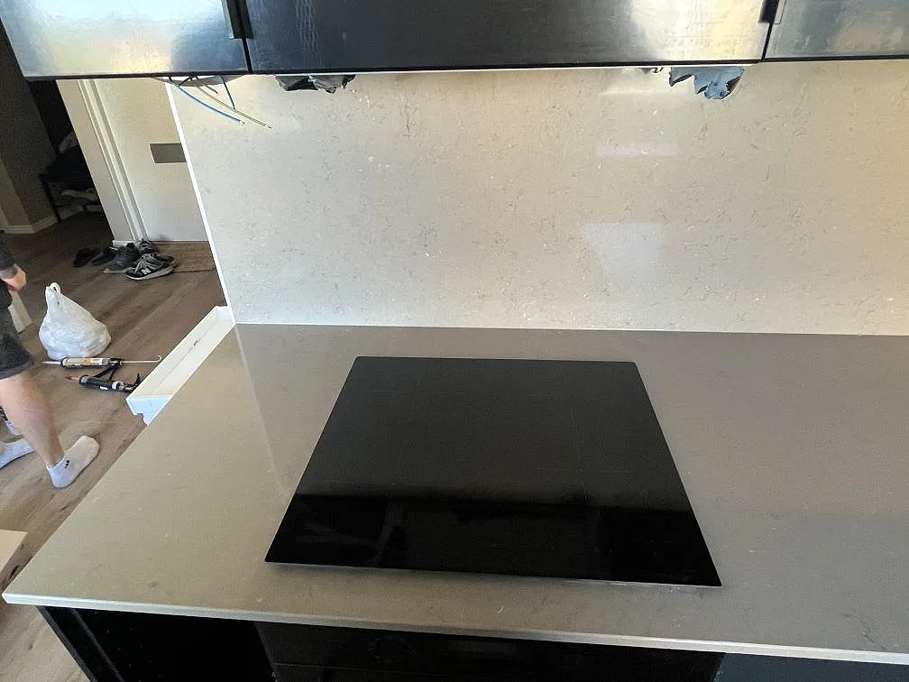 Eye-level vy av polerad Silestone Coral Clay köksbänkskiva med infälld svart induktionshäll och heltäckande stänkvägg i samma sten i ett kök i Malmö.