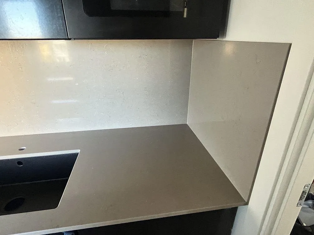 Hörn av polerad Silestone Coral Clay bänkskiva med uppvikt stänkvägg och underlimmad diskho i ett kök i Malmö.