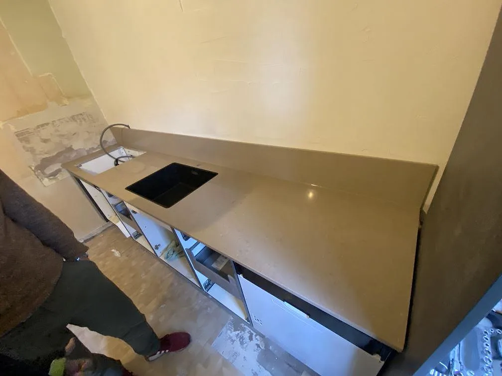 Köksbänkskiva i Silestone Coral Clay, polerad greige kvartskomposit, längs en lång rak bänkrad med uppvikt stänkkant och urtag för diskho och häll i ett kök i Malmö.