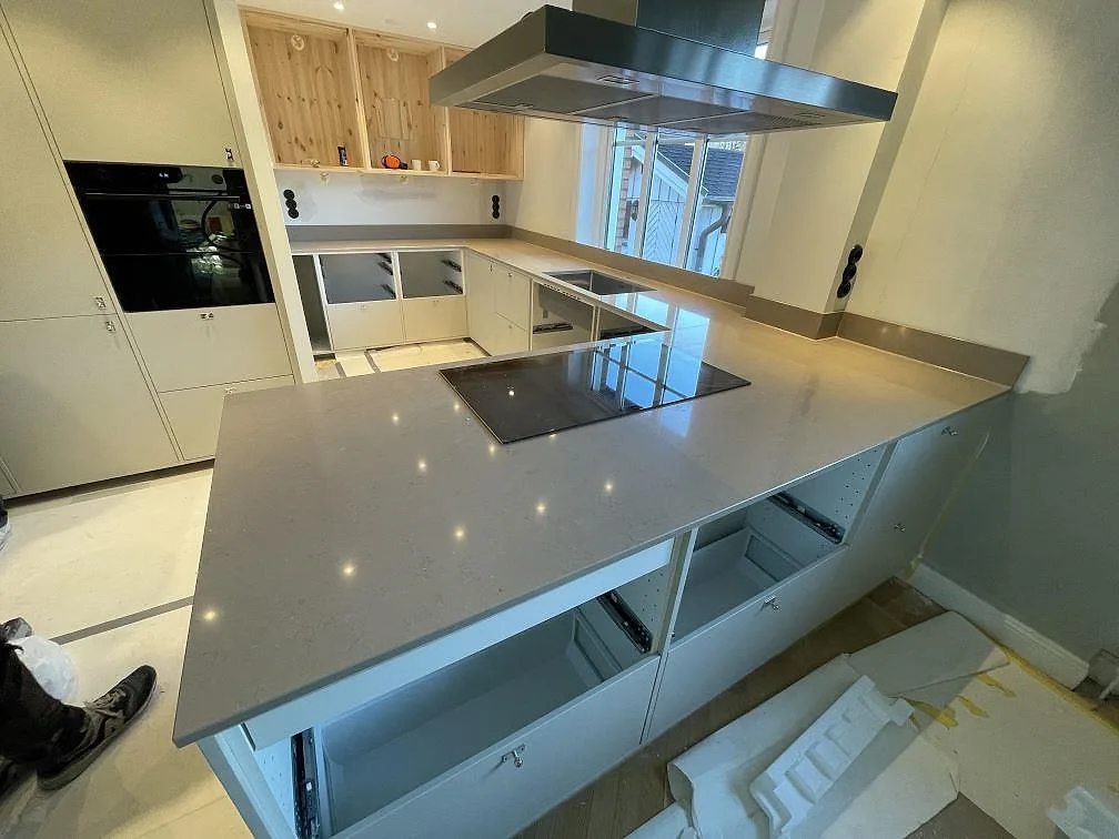 Köksbänkskiva i Silestone Coral Clay, polerad varm greige kvartskomposit, med infälld induktionshäll i en halvö och integrerad fläkt i ett kök under montering i Malmö.