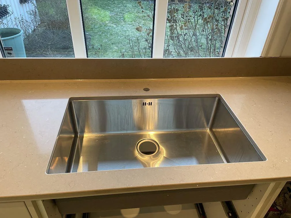 Underlimmad rostfri diskho i en köksbänkskiva av Silestone Coral Clay under ett fönster med utsikt mot trädgården i Malmö.