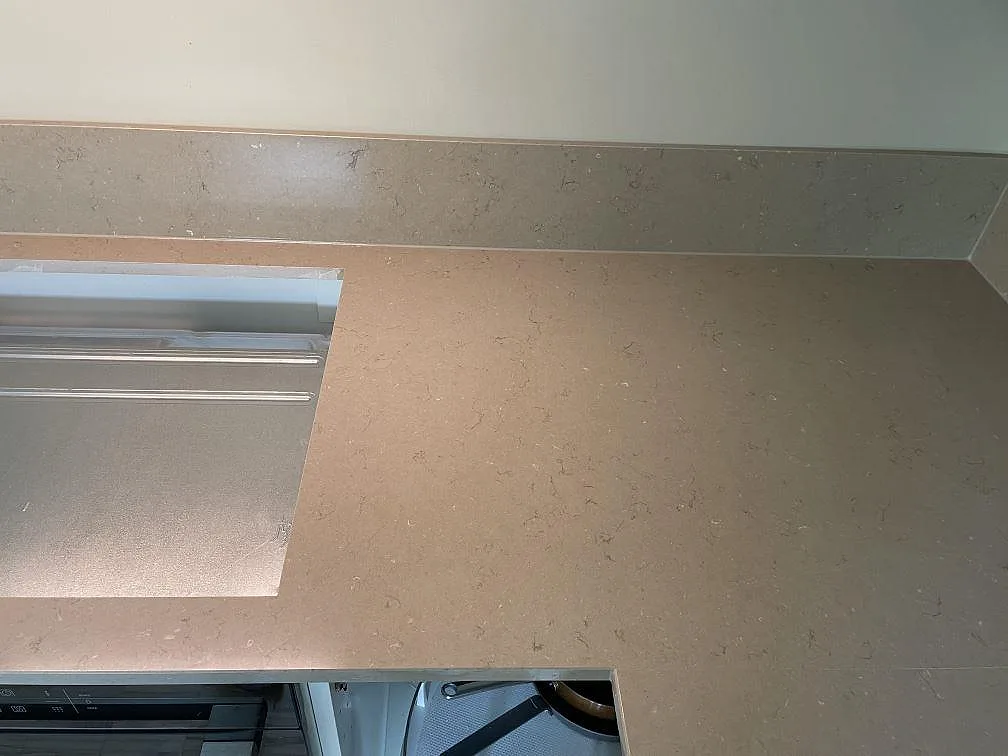 Detalj av varm gråbeige Silestone Coral Clay bänkskiva med hälluttag, stänkkant och synlig polerad yta i Malmö.
