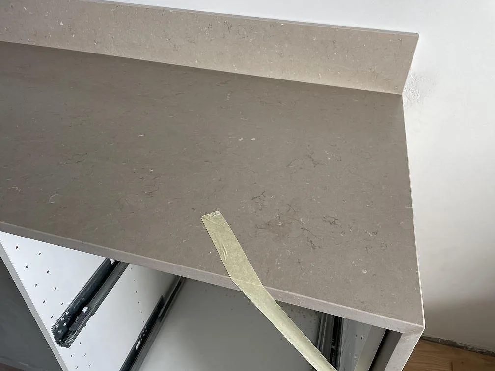 Detaljbild av varm gråbeige Silestone Coral Clay bänkskiva med uppvikt stänkkant och skyddstejp under montering i Malmö.
