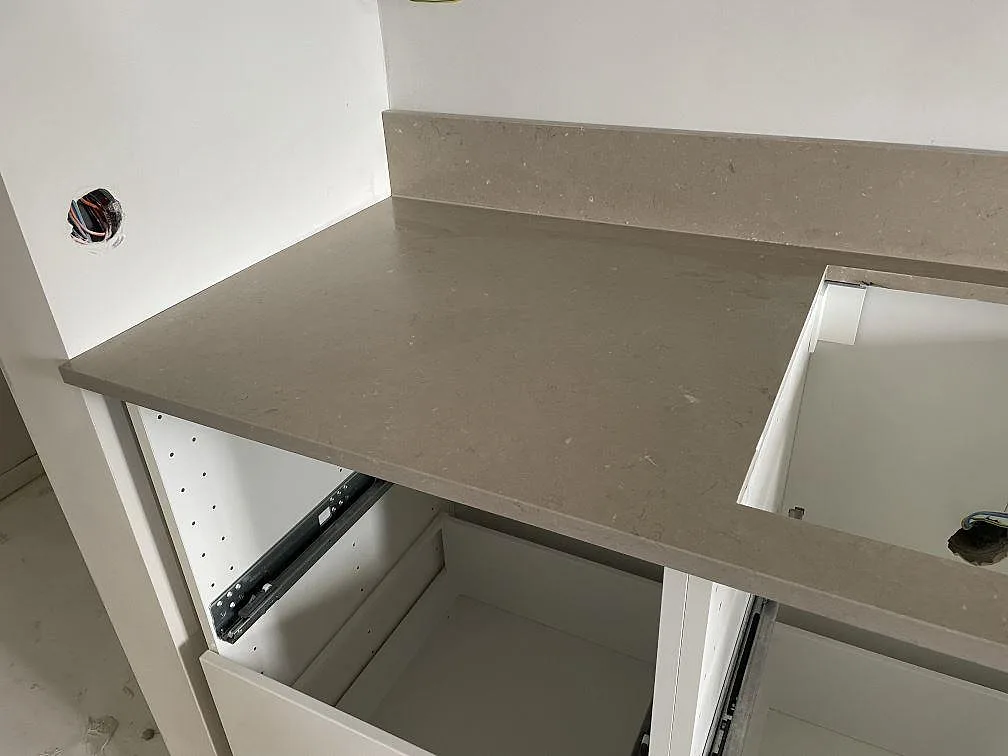 Köksbänkskiva i Silestone Coral Clay komposit med hällurtag, stänkkant och vita köksstommar under montering i Malmö.