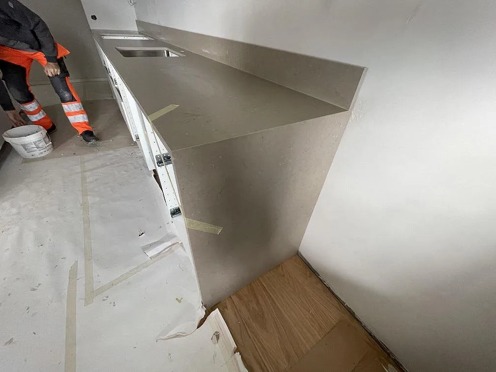 Installerad köksbänkskiva i varm gråbeige Silestone Coral Clay komposit med stänkkant och underlimmad rostfri diskho under montering i Malmö.
