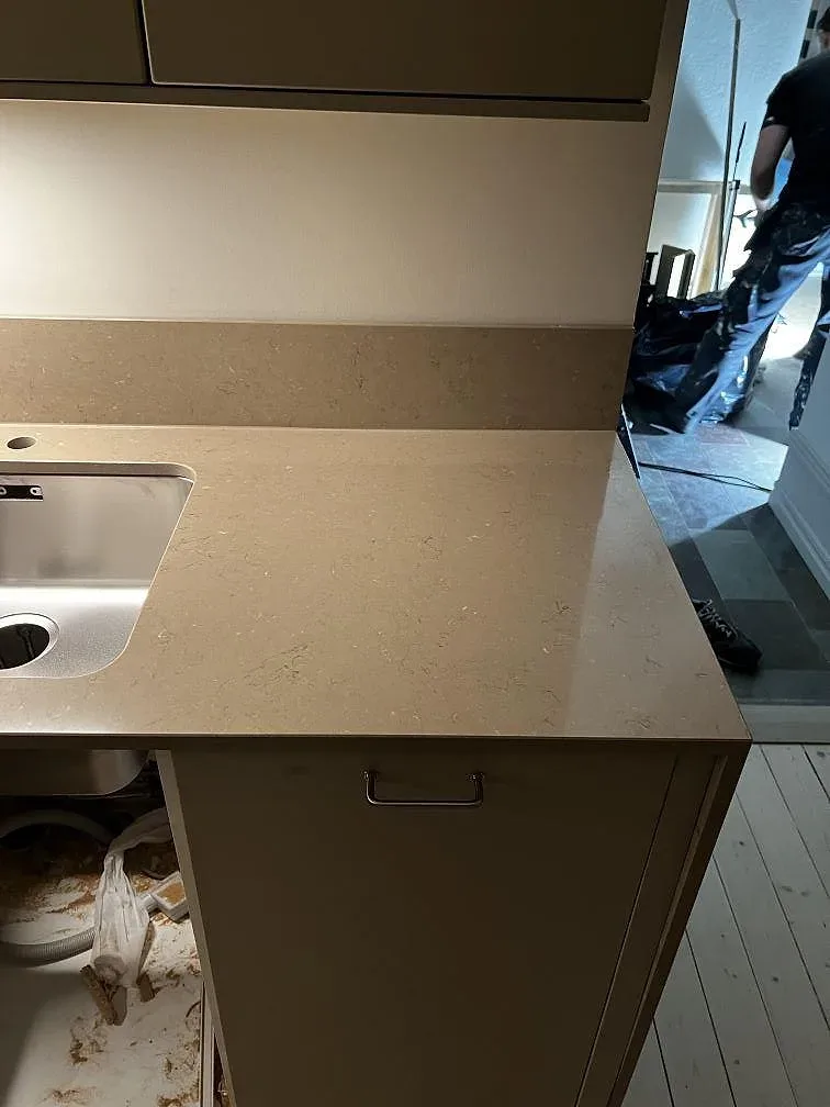 Närbild av varm gråbeige Silestone Coral Clay komposit runt rostfri diskho och uppvikt stänkkant i kök i Malmö.