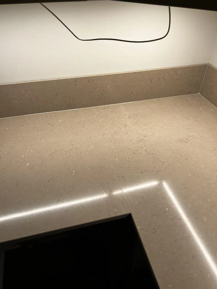 Polerad Silestone Coral Clay arbetsyta med häll, stänkkant och tydliga ljusreflektioner i kök i Malmö.
