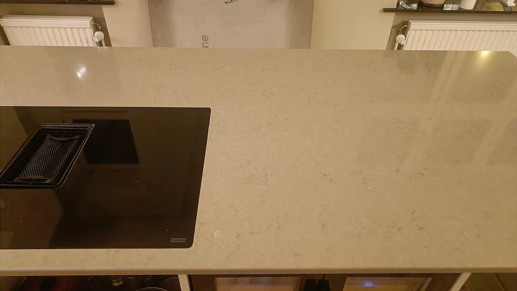 Närbild på polerad Silestone Coral Clay, kvartskomposit, med induktionshäll och ljusa mineralteckningar i Malmö.