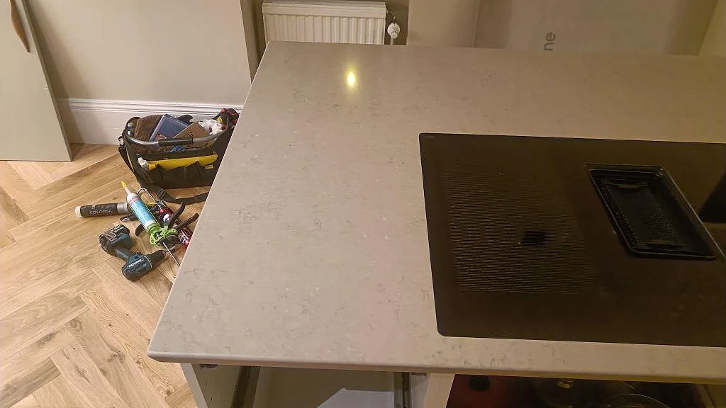Polerad bänkskiva i Silestone Coral Clay med induktionshäll och verktyg vid pågående köksmontering i Malmö.