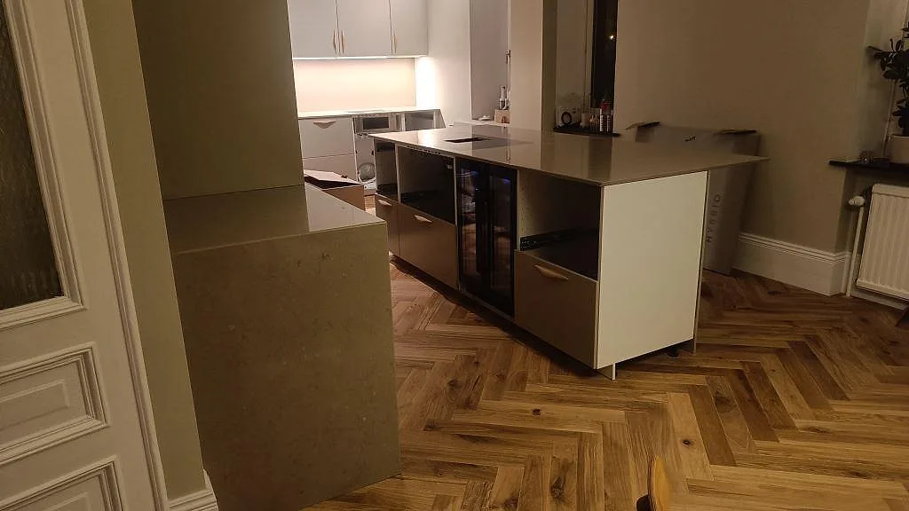 Polerad Silestone Coral Clay på köksö och bänkrad med vit köksinredning och fiskbensgolv i Malmö.