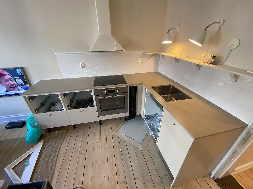 Kök i Malmö med L-formad köksbänkskiva i gråbeige Silestone Coral Clay komposit, vit kakelvägg, rostfri diskho och svart induktionshäll.