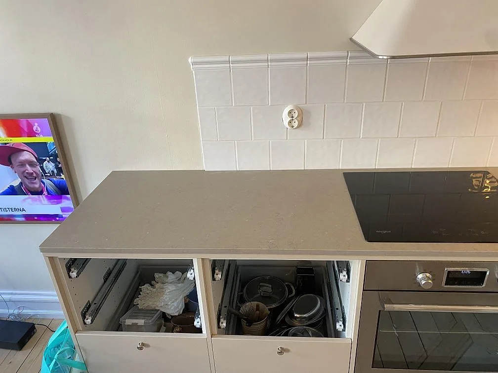 Rak köksbänk i Silestone Coral Clay komposit med matt gråbeige yta, induktionshäll och vit kaklad vägg under montering i Malmö.