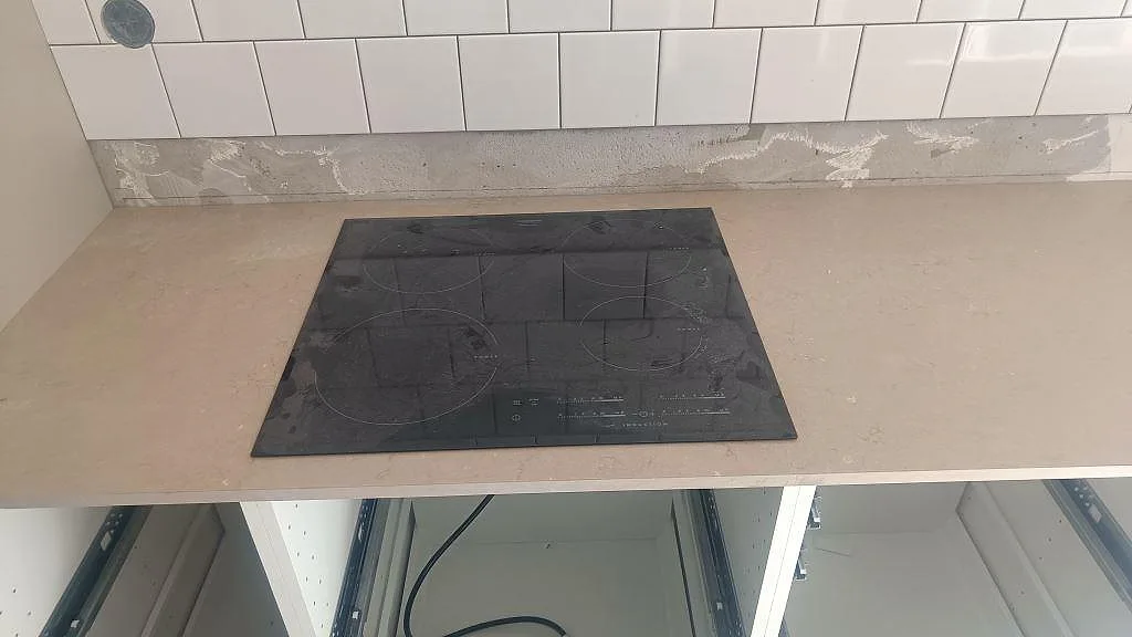 Svart häll infälld i en matt Silestone Coral Clay köksbänkskiva med vit kakelvägg i Malmö.