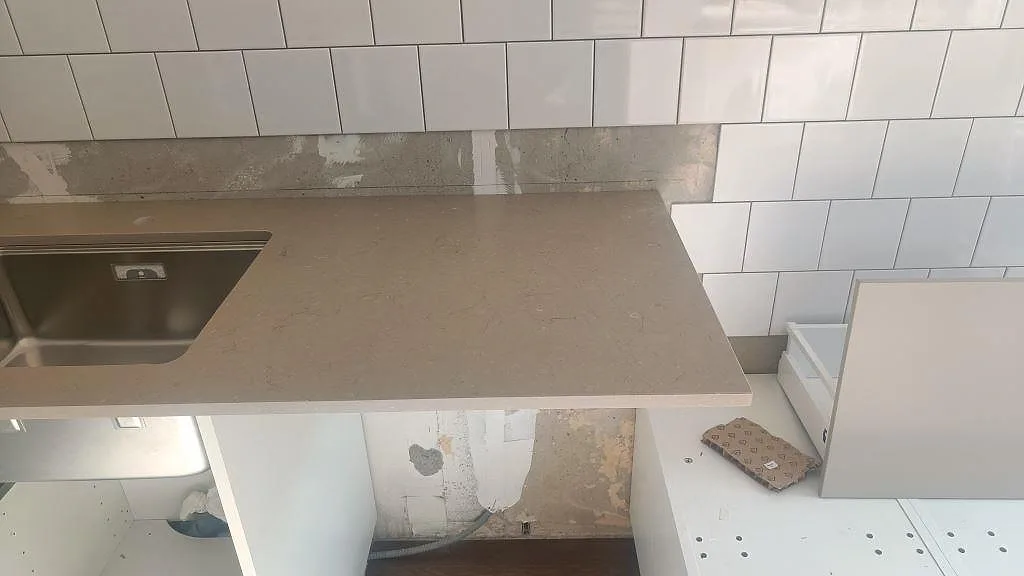 Rak bänkdel i matt Silestone Coral Clay intill underlimmad rostfri diskho och vita köksstommar i Malmö.