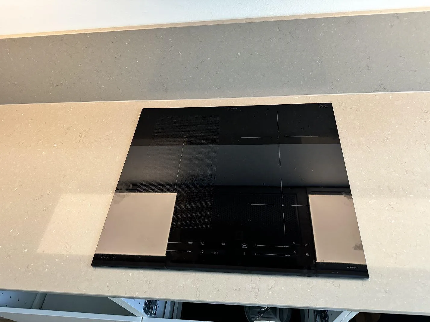 Närbild på svart häll monterad i en polerad köksbänkskiva i Silestone Coral Clay med stänkskydd i Malmö.