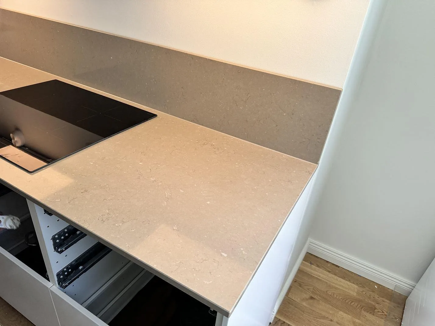 Polerad Silestone Coral Clay som köksbänkskiva och stänkskydd vid svart häll i ett Malmö-kök under montering.