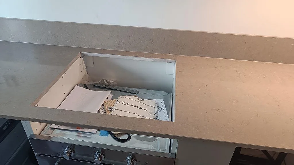Närbild på hällurtag i polerad Silestone Coral Clay med 12 mm stänkkant och öppen köksstomme under montering i Malmö.
