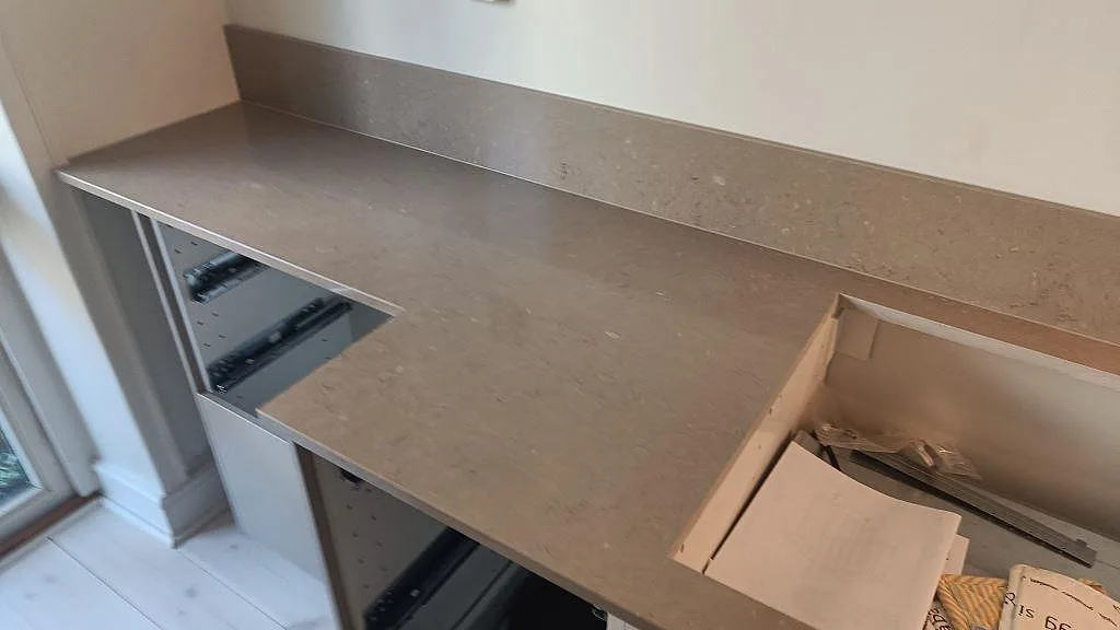 Köksbänkskiva i Silestone Coral Clay, polerad kvartskomposit, med hällurtag, öppet diskhoskåp och 12 mm stänkkant i ett kök i Malmö.